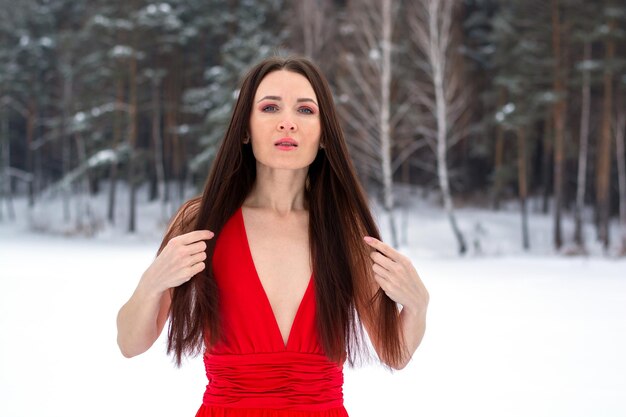 Zdjęcie piękna brunetka dziewczyna w cienkiej czerwonej sukience i boso w zimowym lesie