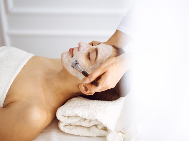 Piękna brunetka kobieta korzystających z maski kosmetycznej z zamkniętymi oczami. Relaksujący zabieg w koncepcji medycyny i centrum spa.