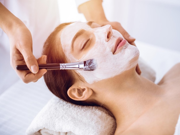 Piękna brunetka kobieta korzystających z maski kosmetycznej z zamkniętymi oczami w centrum słonecznego spa. Relaksująca koncepcja leczenia i medycyny.