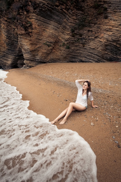 Piękna brunetka kobieta relaksuje się na bezludnej plaży między klifami