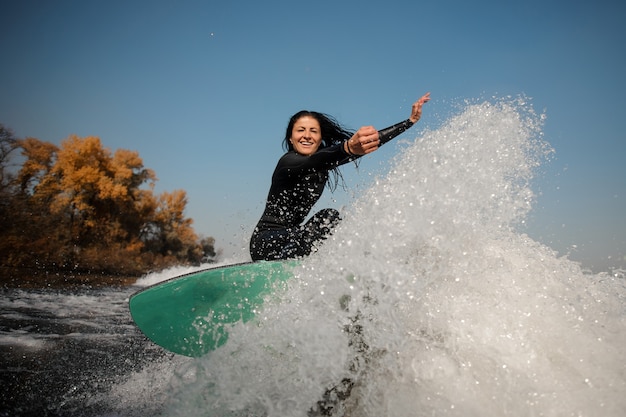 Zdjęcie piękna brunetka kobieta w białym stroju kąpielowym, skacząca na zielonym wakeboardzie na zginane kolana