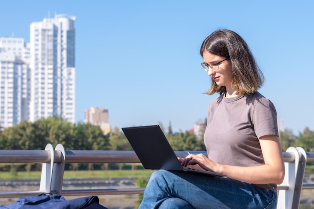 Piękna brunetka studentka w okularach używa laptopa na ulicy Piękna studentka używa laptopa