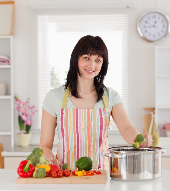 Piękna brunetki kobieta pozuje podczas gdy gotujący warzywa