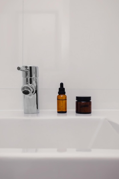 Piękna butelka produktu kosmetycznego w brązowym szkle na białym zlewie w tle łazienki z miejscem na kopię Ekologiczna zrównoważona pielęgnacja skóry Minimalne wnętrze domu Poranna pielęgnacja