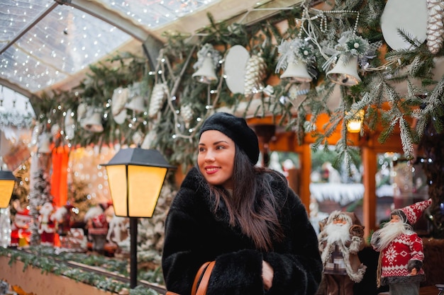 Piękna ciemnowłosa młoda kobieta w eko futrze spaceruje po mieście i robi świąteczne zakupy Nowy Rok Święta Obecne wakacje Zima