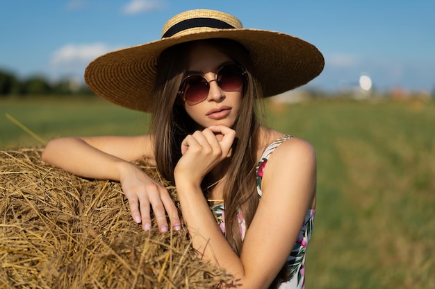Piękna czarująca dziewczyna w sukience i słomkowym kapeluszu na polu w pobliżu stogu siana