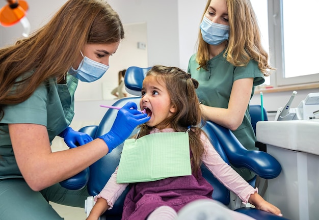 Piękna dentystka ze swoim asystentem w mundurze medycznym patrząca na zęby dzieci