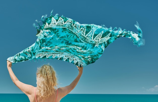 Piękna dojrzała kobieta trzyma pareo na wietrze unoszącej się tkaniny na tle błękitnego słonecznego nieba beztroski na zewnątrz Zdrowy styl życia relaks prosta naturalna przestrzeń