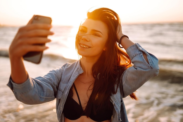 Piękna dziewczyna bierze selfie na plaży o zachodzie słońca Koncepcja relaksującej podróży i letnich wakacji