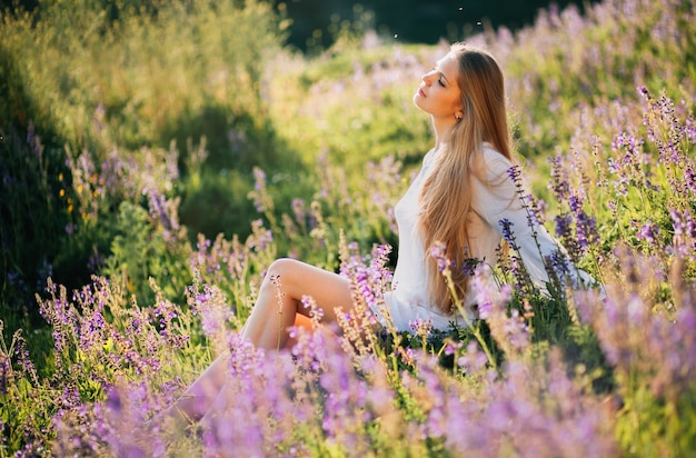 piękna dziewczyna dla słodkich kwitnących szałwii kwiatów w polu o zachodzie słońca.