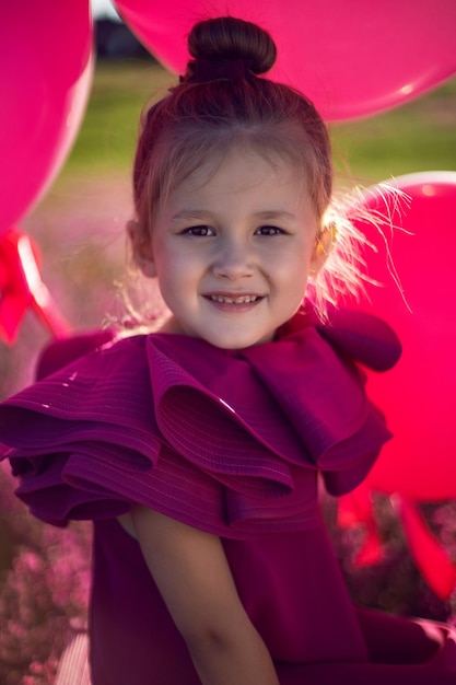 Piękna dziewczyna dziecko w wieku 5 lat siedzi na różowej drabinie w różowej sukience w polu z różowymi kwiatami latem o zachodzie słońca