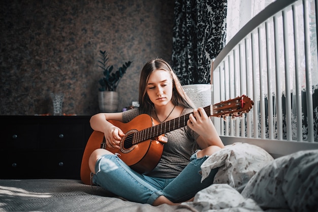 Zdjęcie piękna dziewczyna gra na gitarze w swojej sypialni.