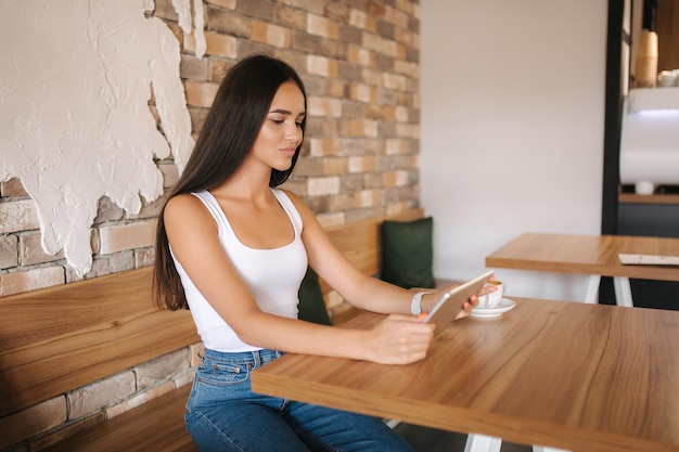 Piękna dziewczyna korzysta z tabletu w kawiarni, ogląda studentkę online w kawiarni za pomocą wifi