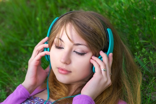 Piękna dziewczyna leżąca na trawie i słuchająca muzyki przez słuchawki w parku