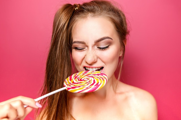 Piękna dziewczyna modelka je kolorowy Lollipop Radosna młoda kobieta z włosami w koński ogon