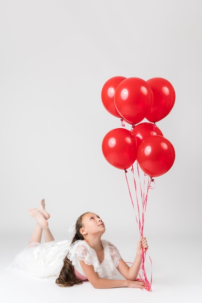 Piękna dziewczyna na przyjęciu urodzinowym, leżąc i trzymając w ręku czerwone balony, patrząc w górę