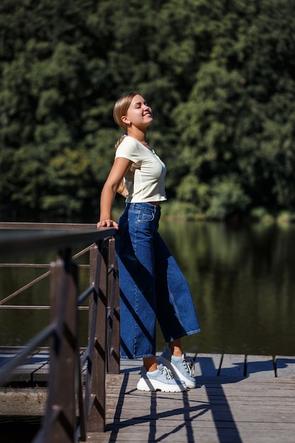 Piękna dziewczyna o europejskim wyglądzie. Młoda kobieta idzie nad rzeką. Ubrany w dżinsy i T-shirt.