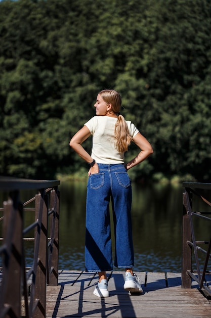 Piękna dziewczyna o europejskim wyglądzie. Młoda kobieta idzie nad rzeką. Ubrany w dżinsy i T-shirt.
