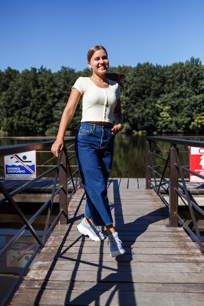 Piękna dziewczyna o europejskim wyglądzie. Młoda kobieta idzie nad rzeką. Ubrany w dżinsy i T-shirt.