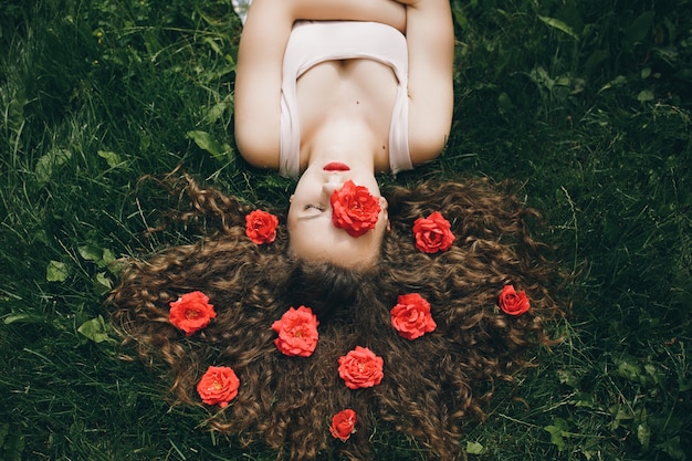Piękna dziewczyna odpoczywa na zielonej trawie z czerwonymi różami we włosach