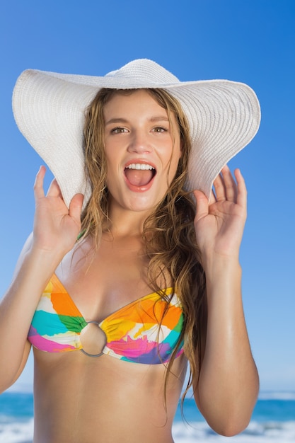 Piękna dziewczyna patrzeje kamerę na plaży w bikini i słomianym kapeluszu