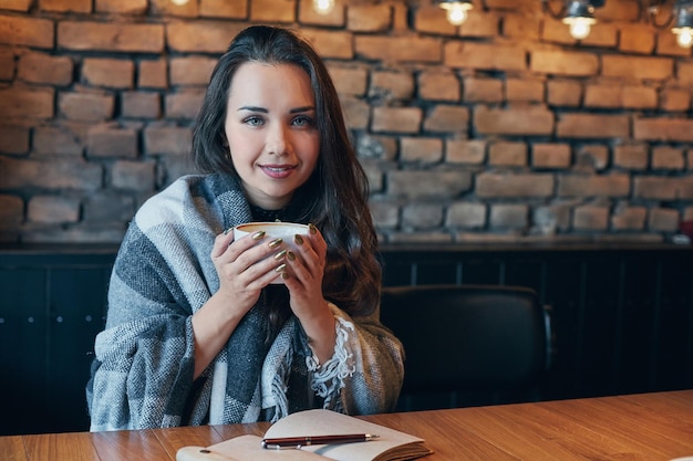 Piękna dziewczyna pijąca kawę w restauracji. Portret młodej damy z ciemnymi kręconymi włosami śniąc zamykając oczy z filiżanką w rękach. Piękna dziewczyna siedząca w kawiarni z filiżanką kawy