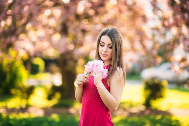 Piękna dziewczyna pozuje do fotografa na tle kwitnących różowych drzew. Wiosna. Sakura.