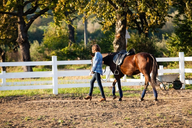 Piękna dziewczyna prowadzi swojego brązowego konia na farmie
