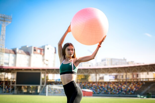 Piękna dziewczyna robi ćwiczenia na fitball na stadionie w słoneczny dzień. Zdrowy styl życia w mieście.