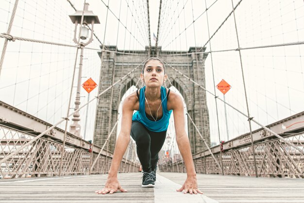 Piękna dziewczyna robi rozciąganiu przy wczesnym porankiem przed biegać. Most Brookliński i panoramę Nowego Jorku w tle