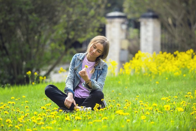 Piękna dziewczyna siedzi na jasnozielonym trawniku z żółtymi kwiatami