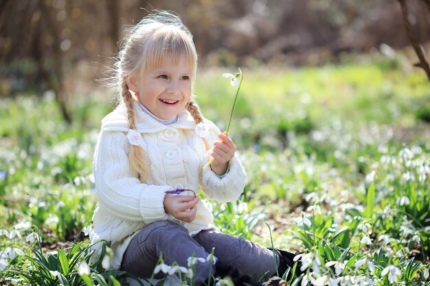 Piękna dziewczyna siedzi na Przebiśniegi łąki kwiat. Piękna mała dziewczynka w białym swetrze z dzianiny spaceruje wiosną po lesie. czas Wielkanocy