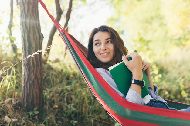 Piękna dziewczyna studentka odpoczynek w parku, leżąc w hamaku i czytając książkę