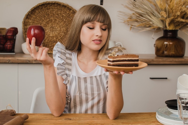 Piękna dziewczyna trzyma w jednej ręce ciasto, a w drugiej jabłko i zastanawia się, co zjeść