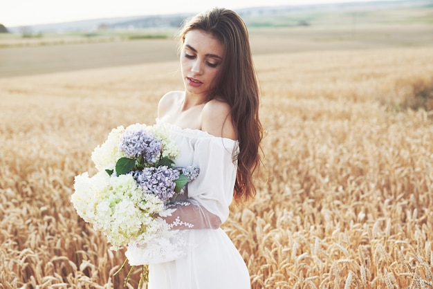 Piękna dziewczyna w białej sukni działa na polu pszenicy jesienią o zachodzie słońca