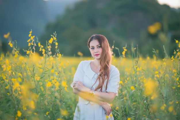 Piękna dziewczyna w białej sukni sfotografowana pośrodku żółtego pola z kwiatami o zachodzie słońca.