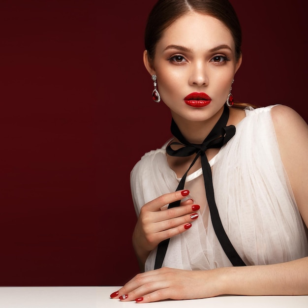 Piękna dziewczyna w białej sukni z klasycznym makijażem i czerwonym manicure Piękna twarz Zdjęcie zrobione w studio