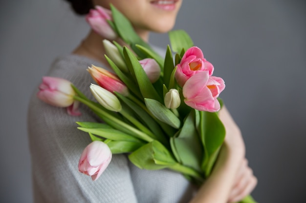 Piękna dziewczyna w błękitnej sukni z kwiatów tulipanami w rękach na lekkim tle