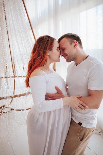 Piękna dziewczyna w ciąży w białej sukni z mężem w studio