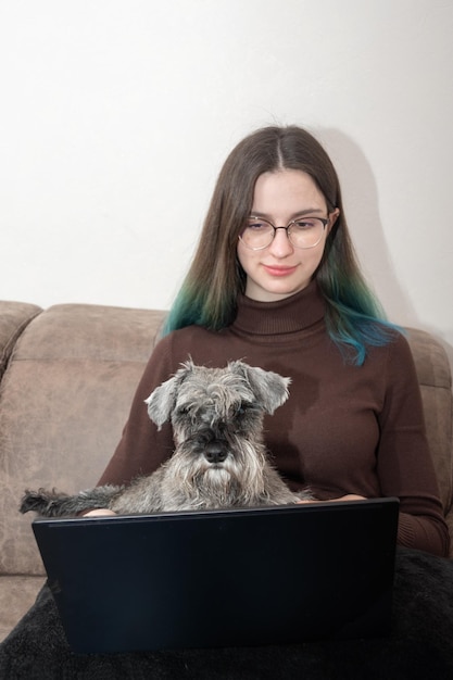 Piękna Dziewczyna W Codziennych Ubraniach Korzysta Z Laptopa I Uśmiecha Się Siedząc Ze Swoim Uroczym Psem Na Zbliżenie Kanapie Zwierzę Patrzy W Kamerę Studentka Studiuje Online Ze Swoim Psem