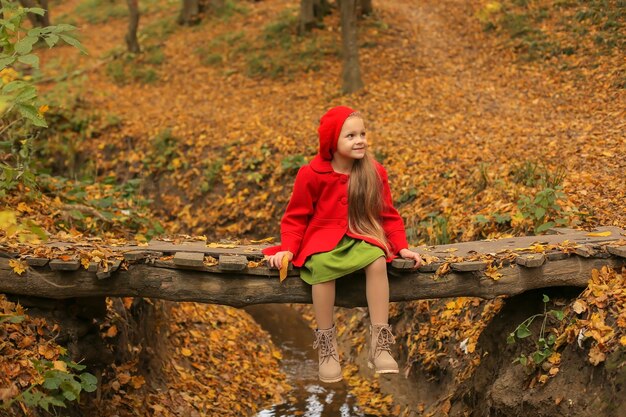 piękna dziewczyna w czerwonym płaszczu i berecie siedzi na moście przez rzekę w jesiennym lesie
