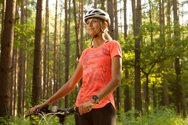 Piękna dziewczyna w jasny pomarańczowy t-shirt, spodenki i kask, jazda w lesie na rowerze