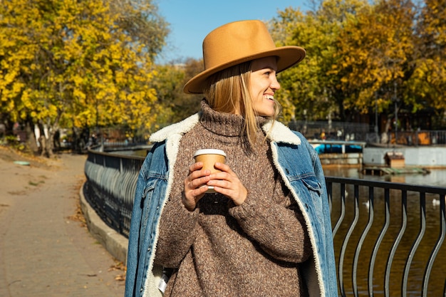 Piękna dziewczyna w kapeluszu chodzi w jesiennym parku z kawą