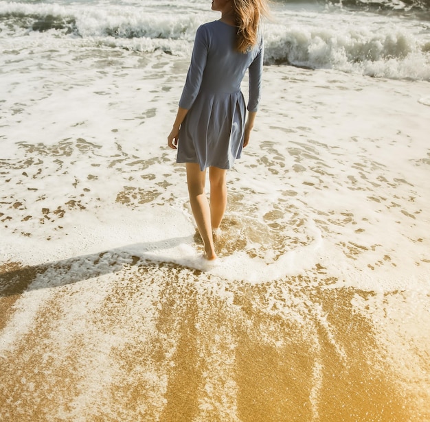 Piękna dziewczyna w niebieskiej sukience spaceruje po plaży Niesamowite letnie zdjęcie Kobieta blisko morza Koncepcja podróży wakacyjnych Szczupłe nogi Ciepła woda oceanu