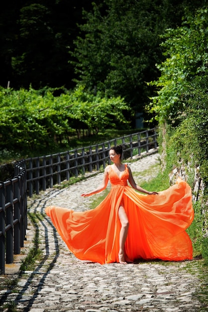 Piękna dziewczyna w niesamowitej powiewającej pomarańczowej sukience stojąca na brukowanej zakrzywionej drodze