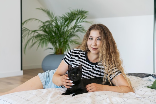 Piękna dziewczyna w pasiastej koszulce leży z ukochanym czarnym kotem na łóżku
