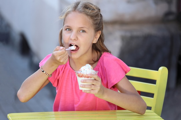 Piękna Dziewczyna W Różowej Koszulce Siedzi Przy żółtym Stole I Je Lody