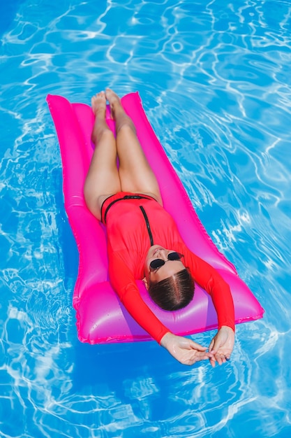 Piękna dziewczyna w różowym stroju kąpielowym relaksuje się na dmuchanym różowym materacu w basenie Szczupła gorąca kobieta w okularach przeciwsłonecznych i strojach kąpielowych opala się Kobieta relaksuje się w luksusowym kurorcie