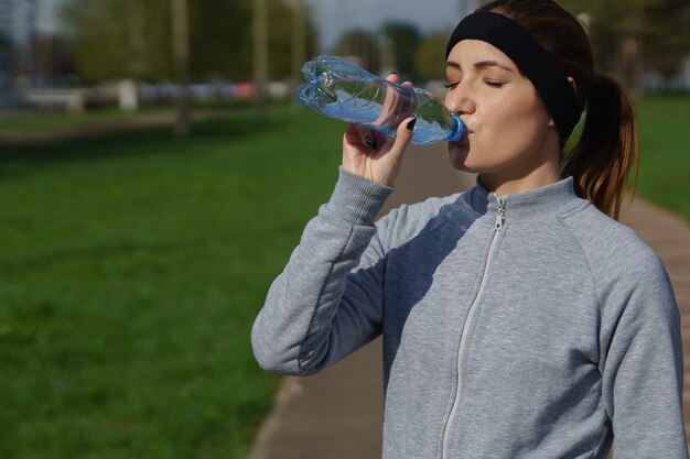 Piękna dziewczyna w sportowej pije wodę. Sport fitness biegacz kobieta po joggingu.