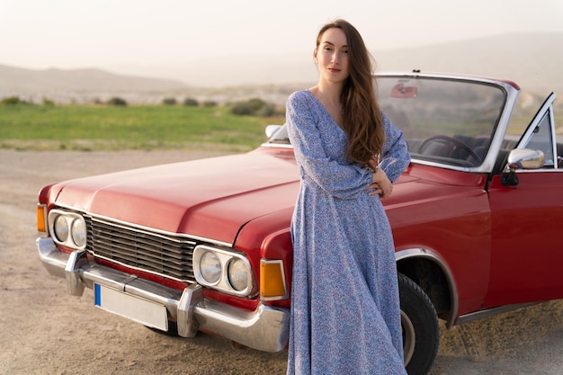 Piękna dziewczyna w stylu retro pozuje w pobliżu zabytkowego czerwonego kabrioletu samochodu